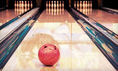 a red bowling ball sitting in the middle of a bowling alley with its skittles down