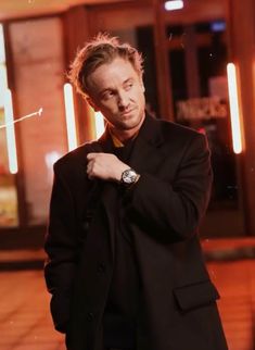 a man in a black suit is posing for the camera with his hand on his tie