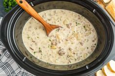 a wooden spoon in a slow cooker filled with soup and bread slices on the side