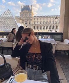 a woman sitting at a table in front of a building with a glass of orange juice