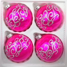 four pink ornaments with silver swirls in a box