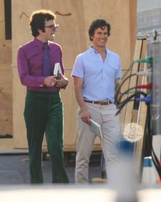 two men standing next to each other in front of a wooden structure with tools on it