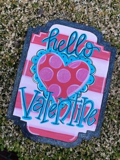 a hello valentine sign laying on top of some green grass with the word hello valentine painted on it