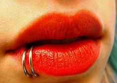 a woman's lips with red lipstick and silver ring on her lip, close up