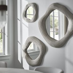 three circular mirrors mounted on the wall above a table with chairs in front of it