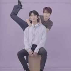 two young men sitting on top of each other in front of a purple background,