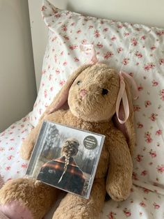 a brown teddy bear sitting on top of a bed next to a cd case and pillow