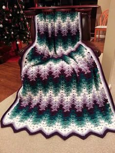 a crocheted blanket sitting on top of a wooden table next to a christmas tree