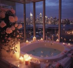 a bathtub with candles and flowers in front of a large window overlooking the city