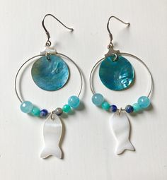 These medium-sized hoop earrings combine small round beads in aquamarine, sodalite and agate with a round sequin in turquoise blue mother-of-pearl and a small fish pendant in white mother-of-pearl. Light, colorful and with a marine theme, they are perfect for summer! The clip is made of 925 silver. Diameter of the metal circle 35mm. Mother-of-pearl is an organic material produced by shellfish. With feminine and maternal symbolism, it is reputed to promote charm, contact and appeasement. It is al Handmade Blue Mother Of Pearl Jewelry, Blue Hoop Earrings With Natural Stones, Detergent Product, Pearl Light, 2017 Trends, Appeasement, Creole Earrings, Marine Theme, Pearl Jewels