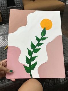 a person holding up a piece of art with a plant painted on it's side