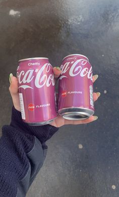 a person holding two cans of coca - cola in their hands, one is pink and the other is green