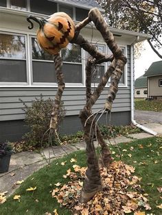 a spider made out of branches with a pumpkin on it's head in front of a house