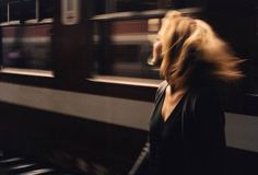 a blurry photo of a woman standing in front of a train station with her hair blowing in the wind