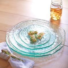 there is a glass plate on the table with napkins next to it and a jar full of honey