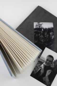 an open book sitting on top of a white table next to two pictures and a black and white photo