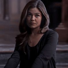 a woman sitting on the ground with her hand in her pocket and looking at the camera