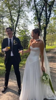 a bride and groom are walking down the road holding champagne flutes in their hands,