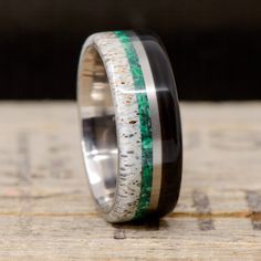 a wedding ring with green and white inlays on the inside, sitting on top of a piece of wood