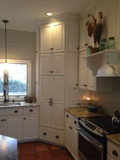 a kitchen with white cupboards and an oven in it's center island next to a window