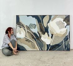 a woman sitting on the ground next to a large painting with white flowers in it