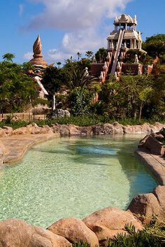 a large water slide in the middle of a pool surrounded by rocks and palm trees