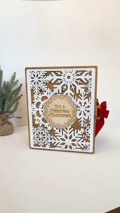 a white and gold christmas card with snowflakes on it, next to a potted plant