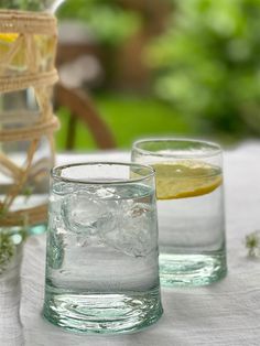 two glasses filled with water and lemon on top of a white tablecloth covered table