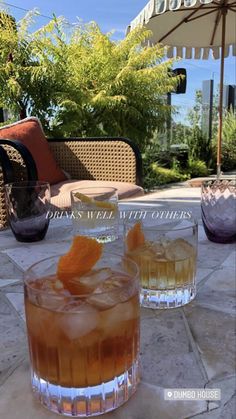 two glasses filled with drinks sitting on top of a stone floor next to an umbrella