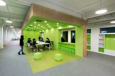 people are sitting at tables in an open office space with bright green walls and flooring