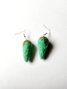 two green felted objects are hanging from silver earwires on a white surface