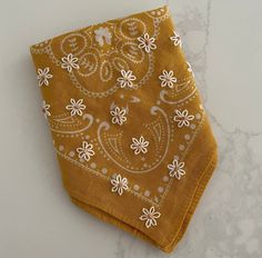 a yellow bandana with white flowers on it sitting on a marble countertop next to a pair of scissors