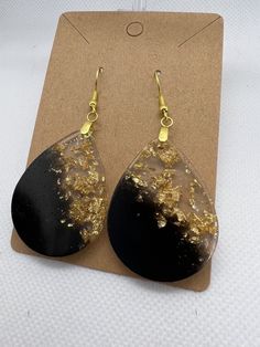 black and gold drop earrings sitting on top of a piece of brown paper next to a card