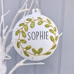 a personalized ornament hanging from a white christmas tree with green leaves on it