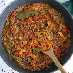 a skillet filled with meat and vegetables on top of a table next to a wooden spoon