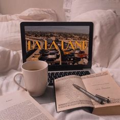 an open laptop computer sitting on top of a bed next to two books and a cup