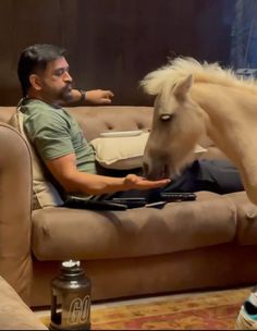 a man sitting on a couch petting a horse