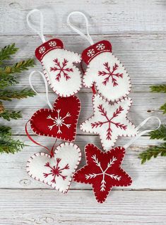 four red and white ornaments hanging on a wooden table next to evergreen branches with snowflakes