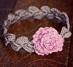 a crocheted headband with a pink flower on the top and gray flowers on the bottom