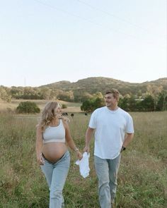 a man and woman walking through a field with a baby bump in their stomachs