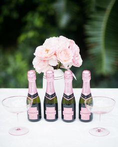 four bottles of champagne and three wine glasses on a table with flowers in the background