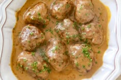 a white plate topped with meatballs covered in gravy and garnished with parsley