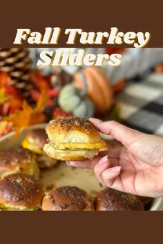 a person holding up a hamburger in front of other sliders on a tray with fall leaves