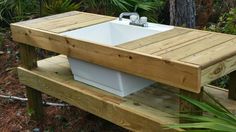 a wooden bench with a white sink on it's side in front of some trees