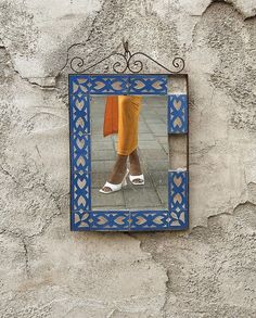 a woman's feet in white shoes are reflected in a blue frame on a stone wall