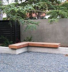 a wooden bench sitting in the middle of a graveled area next to a tree