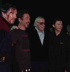 three men standing next to each other in front of a black background with one man wearing sunglasses and the other smiling