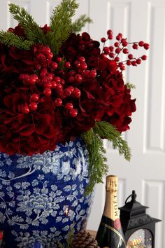 a blue vase filled with red flowers next to bottles of champagne and pineconi