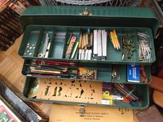 an old green metal box filled with lots of books and pencils on top of a wooden table