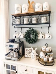 a coffee bar with cups and mugs on the shelf above it, along with other kitchen items